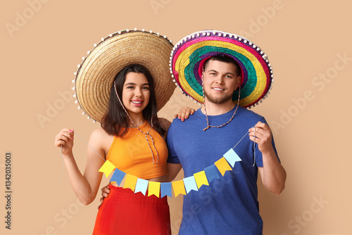 Beautiful young happy couple in sombrero hats with garland on beige background. Cinco de Mayo celebration
