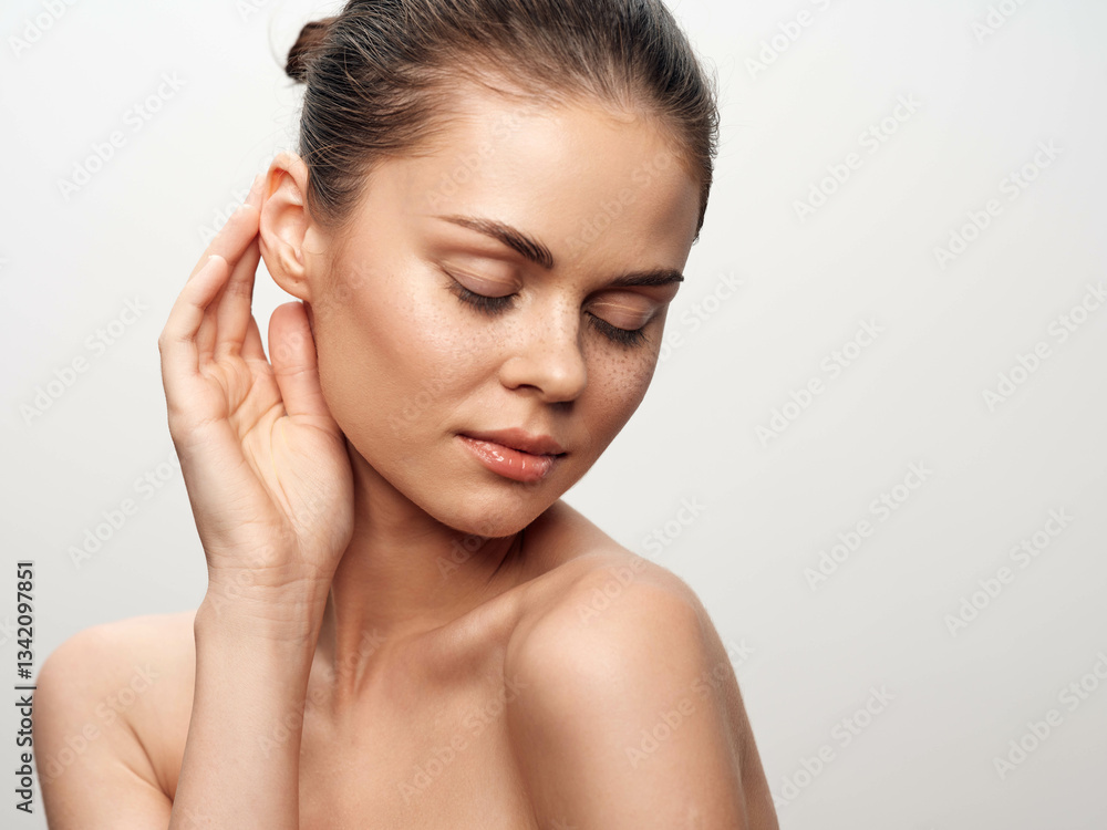 Portrait of a beautiful young woman gently touching her ear with her hand against a white background Portrait of a beautiful young woman gently touching her ear with her hand against a white background
