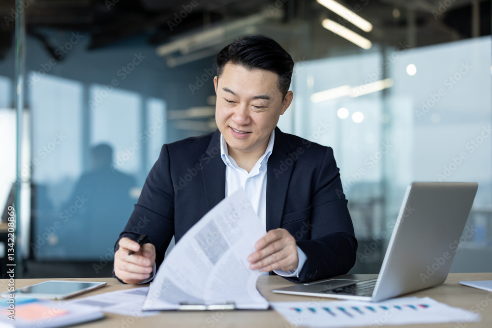 Asian young male businessman working in office at desk with papers, signing documents, analyzing and conducting examination Asian young male businessman working in office at desk with papers, signing documents, analyzing and conducting examination