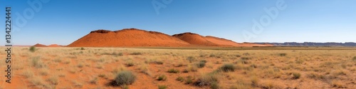 A desert landscape with a large hill in the background. The sky is clear and blue. Concept of vastness and emptiness, with the lone hill as a reminder of the natural beauty and power of the desert