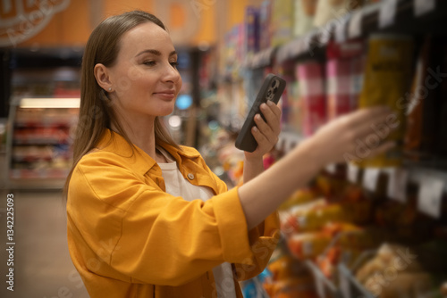 A woman wearing a yellow top chooses cornflakes from a shelf in a grocery store, surrounded by colorful cereal boxes. She carefully scans the options, showcasing her preferences.