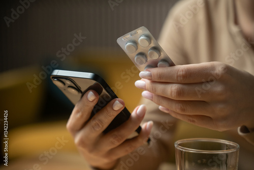 A person examines a blister pack of medication while using a smartphone, indicating a moment of multitasking in a cozy indoor setting during the afternoon hours.