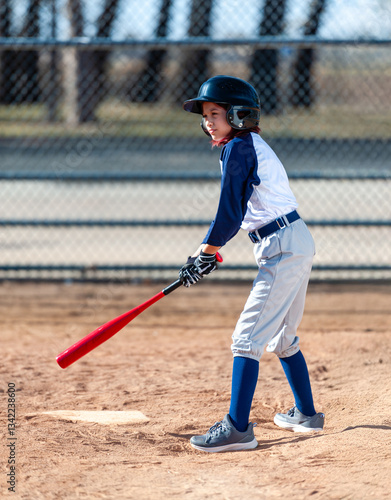 Young girl in little league baseball uniform with bat and helmet at home plate