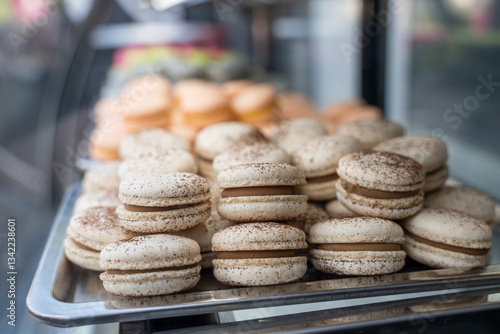 Large amount of pink macaron dessert cakes in refrigerator with glass display case, reflection and glare of glass are visible