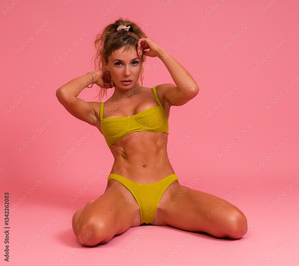 Obraz premium Slender sexy woman in a swimsuit posing while sitting on her knees on a pink background.