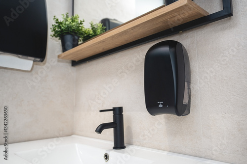  Black dispenser for electronic liquid soap anddispenser for paper towels in a modern bathroom.