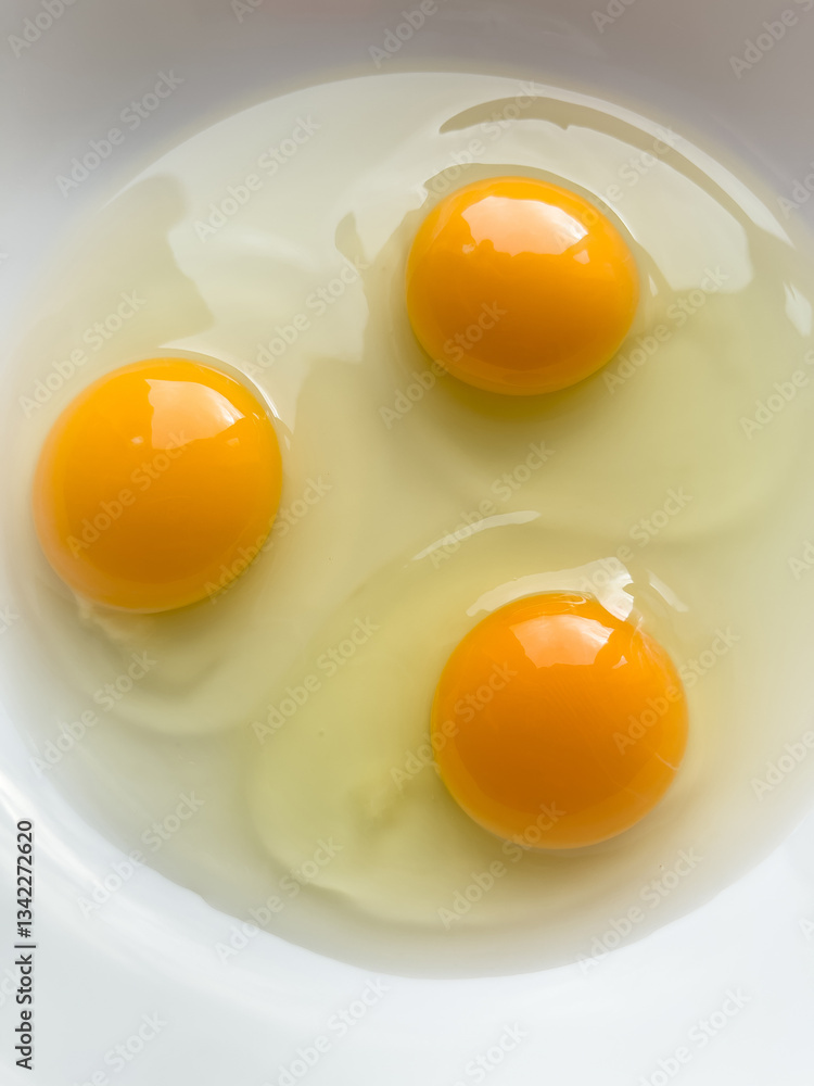 Three bright yellow raw chicken eggs in a white bowl. Three bright yellow raw chicken eggs in a white bowl.