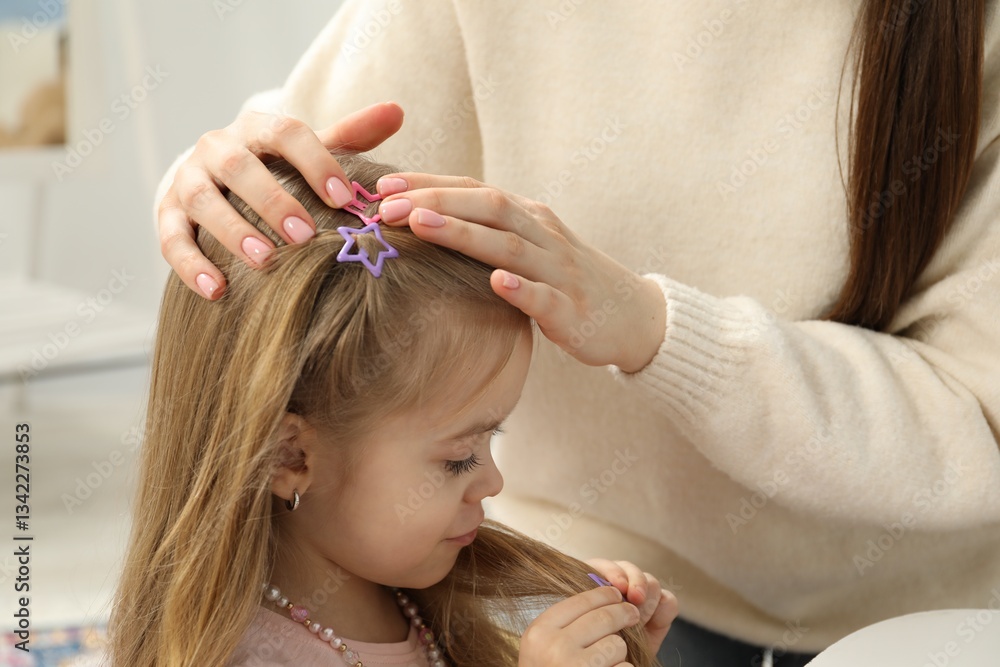 Naklejka premium Mom putting cute accessories onto her daughter's hair at home, closeup