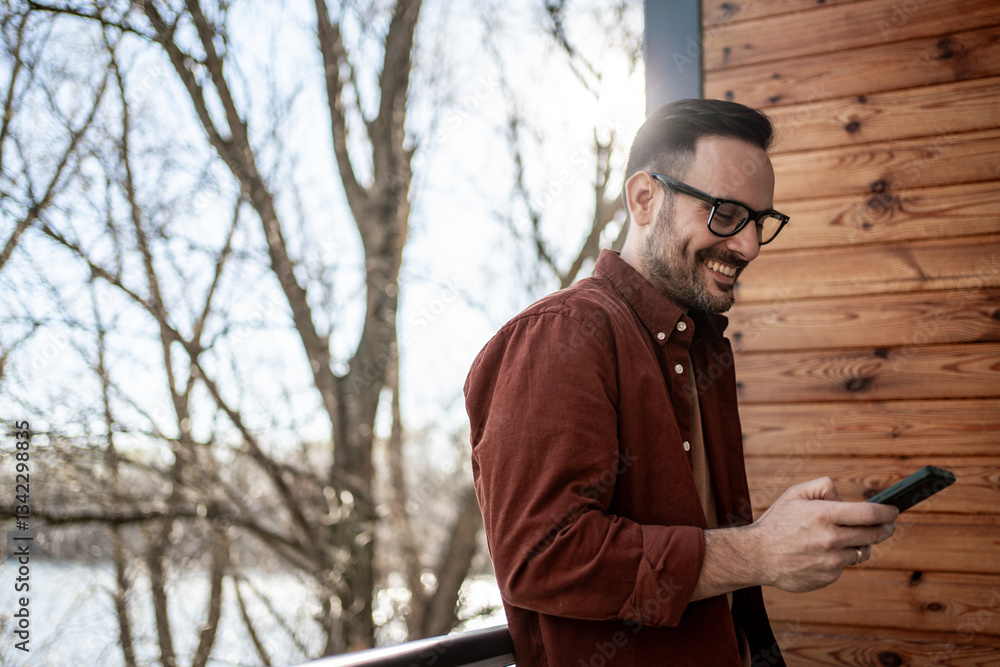 Smiling architect using smartphone on balcony overlooking river Smiling architect using smartphone on balcony overlooking river