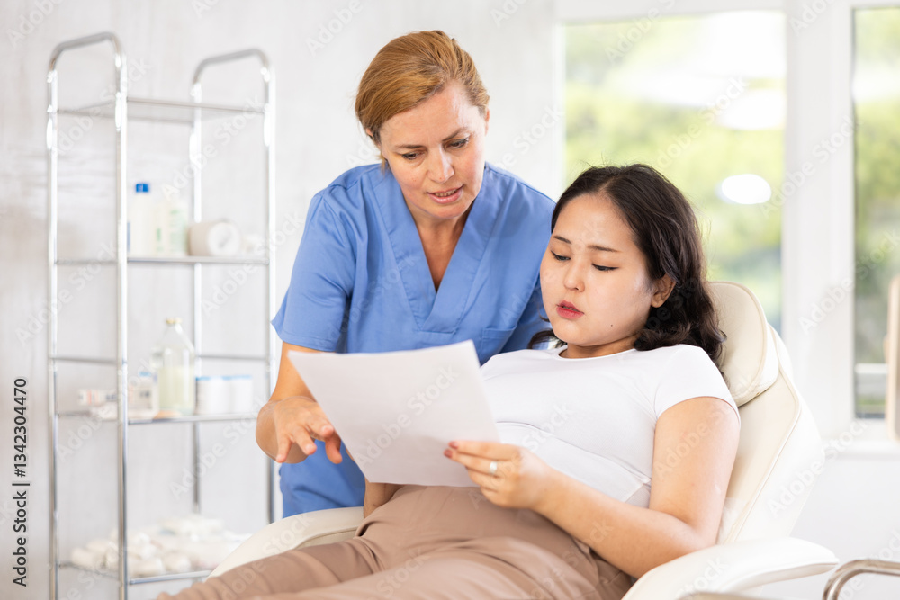 European doctor registering asian woman to cosmetology procedures in medical chair European doctor registering asian woman to cosmetology procedures in medical chair