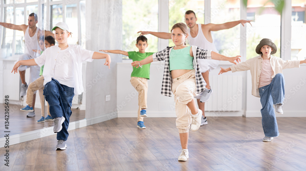 Obraz premium Emotional tween girl dancer rehearsing modern krump dance moves during group workout in kids studio under guidance of male instructor