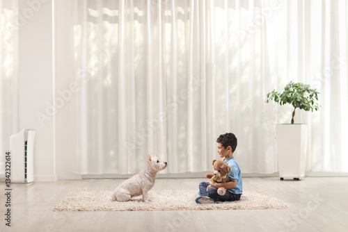 Boy sitting on a carpet and playing with a westie terrier