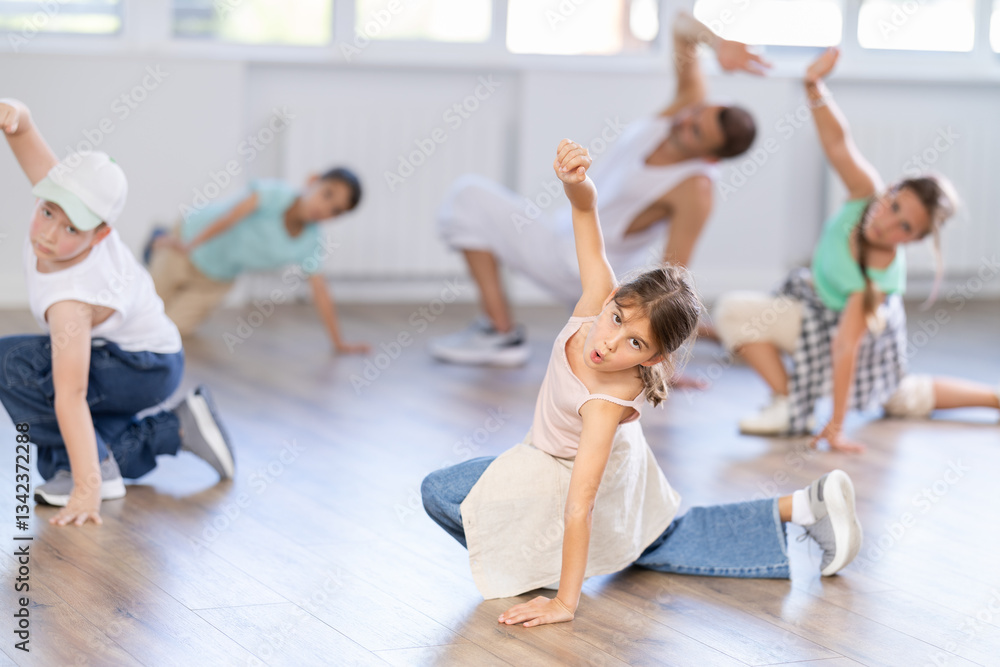 Obraz premium Cheerful sports preteen girls and boys hip hop dancers doing dance workout on floor with male trainer during group class at dance studio