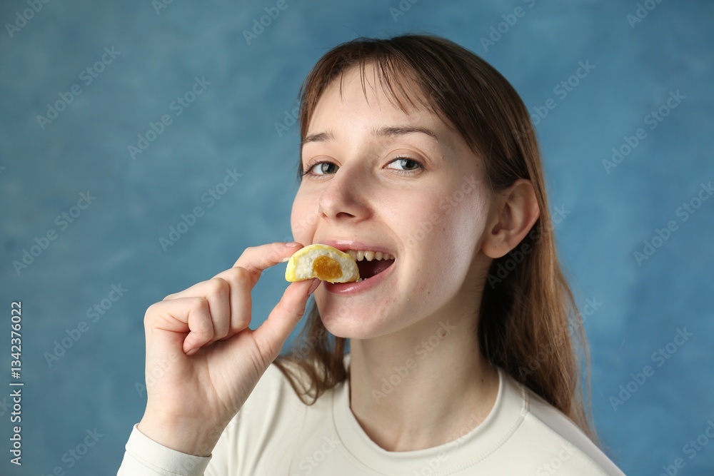 Beautiful woman eating tasty mochi on blurred blue background Beautiful woman eating tasty mochi on blurred blue background