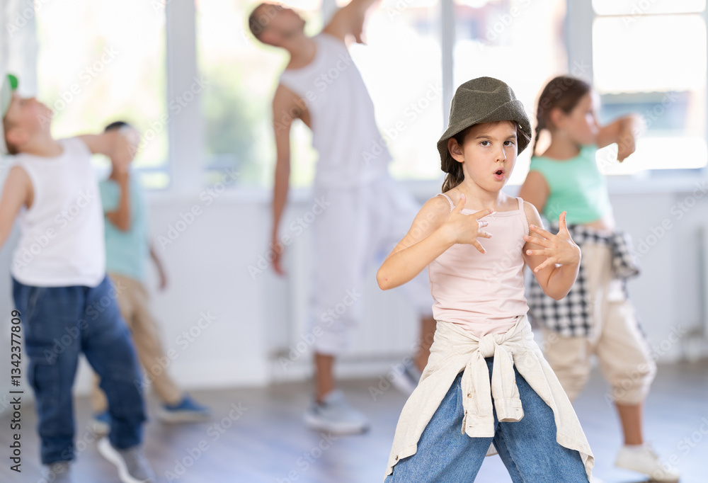 Energetic preteen girl practicing hip hop choreography in well-lit dance studio alongside peers and young male instructor Energetic preteen girl practicing hip hop choreography in well-lit dance studio alongside peers and young male instructor