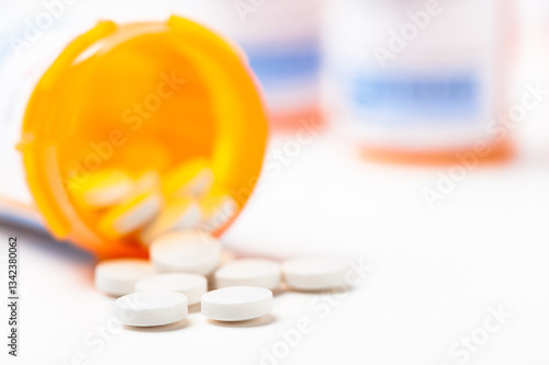 Round white prescription medication medicine pill tablets spilling from a bottle with numerous full bottles in background