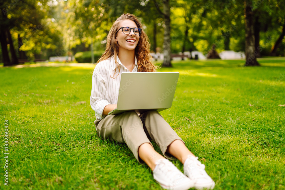 Young woman sitting on grass using laptop working remotely in summer park. Concept for education, business, blog or freelance Young woman sitting on grass using laptop working remotely in summer park. Concept for education, business, blog or freelance