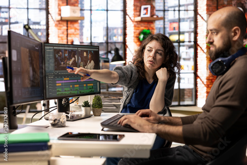 Video editors team working with AI chatbot and montage maker software, editing a background video and mixing clips on dual monitors. Professional man and woman in creative process.