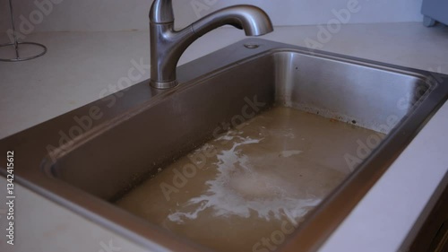 The stainless steel sink filled with murky, brown water, a drainage issue, clogged pipes, or contaminated water supply. Dirty water is coming back to the sink.