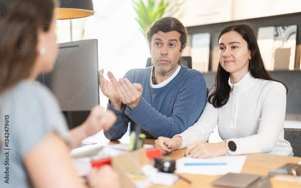 Obraz premium Married couple discusses with the store manager the size of the kitchen set, the quality of materials and delivery times. Buyers order new living room furniture for an apartment after renovation