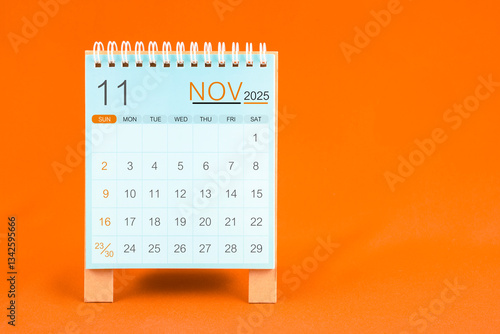 November 2025 desk calendar stand on orange textile background.