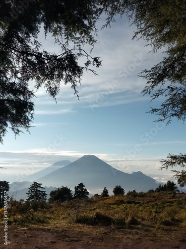 Breathtaking views of the majestic volcanoes of Mount Sindoro and Mount Sumbing towering above the clouds, framed by lush greenery in the morning light from the summit of Mount Prau.
