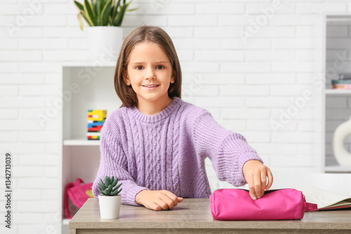 Cute little happy girl with pencil case sitting at home