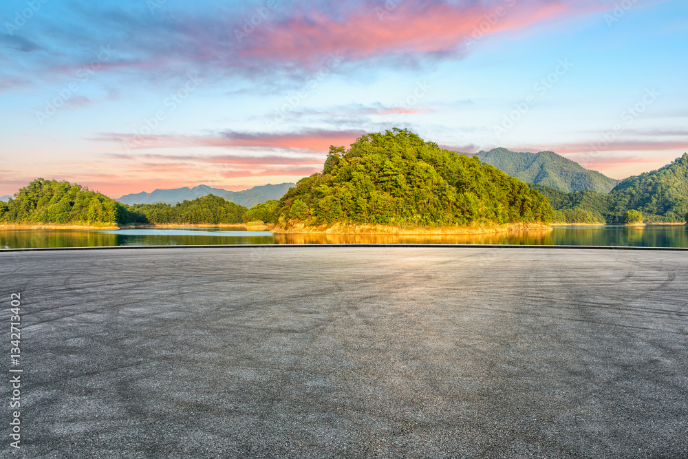 Asphalt road and lake with green mountain scenery at sunset