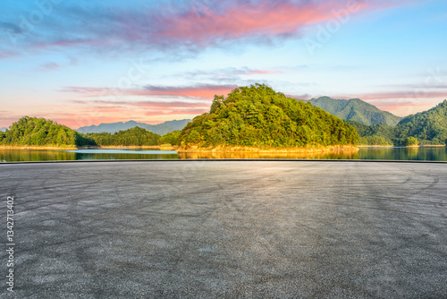 Asphalt road and lake with green mountain scenery at sunset