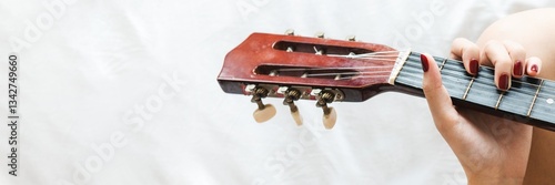 Close-up of a person playing a guitar. Hands strumming guitar strings. Guitar neck and tuning pegs visible. Guitar and music focus. Playing guitar with red nails. Woman playing acoustic guitar.