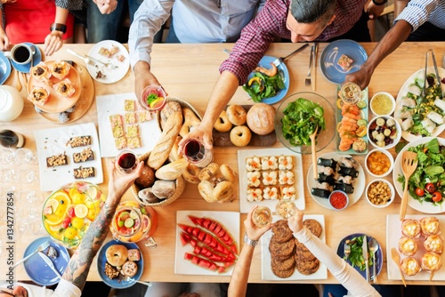 Obraz na płótnie Top view of a diverse group enjoying a meal. People share food, toast drinks, and celebrate. A variety of dishes and drinks on a wooden table. Buffet table with delicious food photo from top view. w salonie