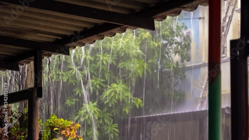 Heavy rain pouring from a roof's edge, blurring the green foliage in the background, creating a tranquil and serene atmosphere