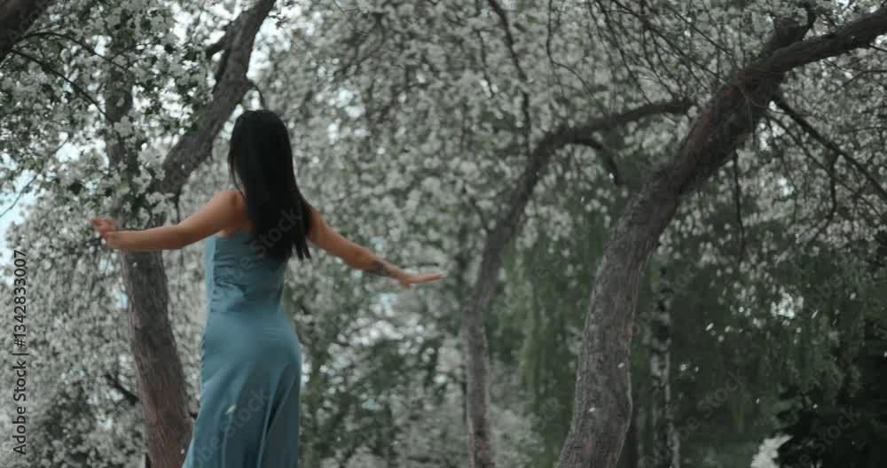 Elegant woman in flowing blue dress moving gracefully among blossoming trees, embodying natural beauty and serenity within peaceful park landscape during springtime Elegant woman in flowing blue dress moving gracefully among blossoming trees, embodying natural beauty and serenity within peaceful park landscape during springtime