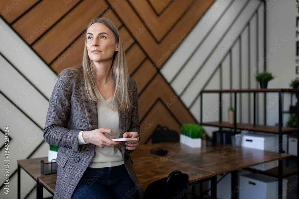 Business professional sitting at a modern workspace, contemplating while holding a smartphone during the day Business professional sitting at a modern workspace, contemplating while holding a smartphone during the day