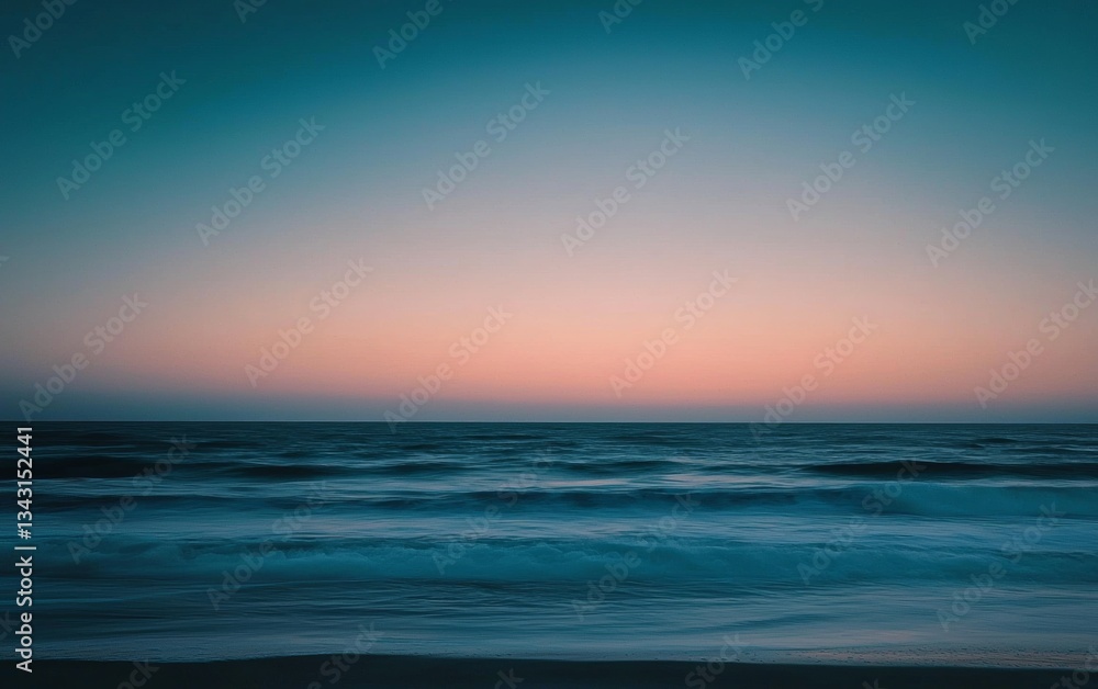 Obraz premium Calm ocean waves and vibrant sunset sky create a peaceful atmosphere at the beach in quiet evening light