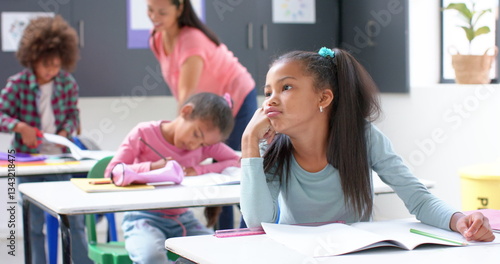 фотографія In school, girl daydreaming at desk while classmates and teacher working