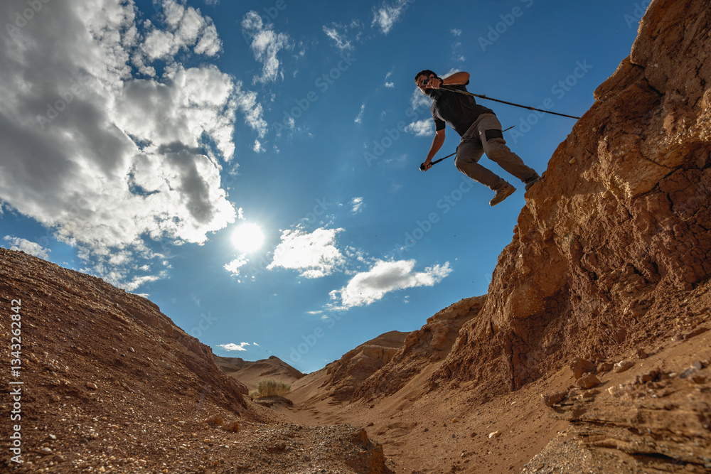 Obraz premium A pioneer traveler with trekking poles in his hands makes a jump in a canyon located in the Gobbi Desert in Mongolia.