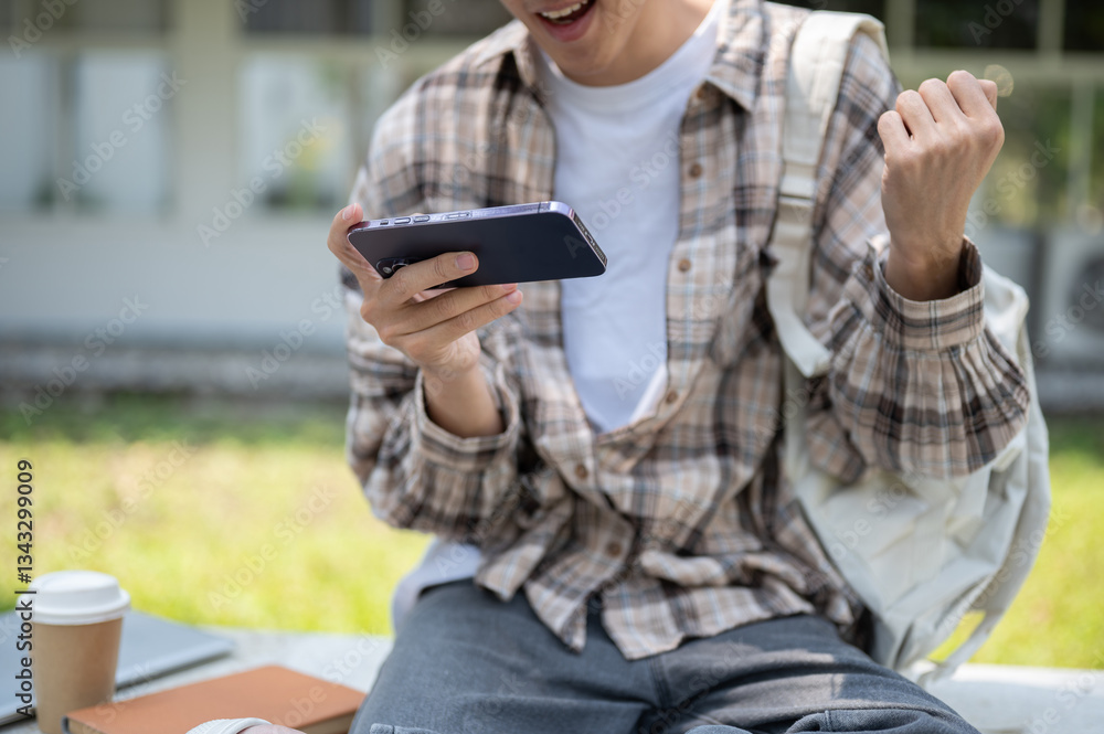 Close up of a man looking at phone and make a fist while sitting with coffee and book on park bench Close up of a man looking at phone and make a fist while sitting with coffee and book on park bench