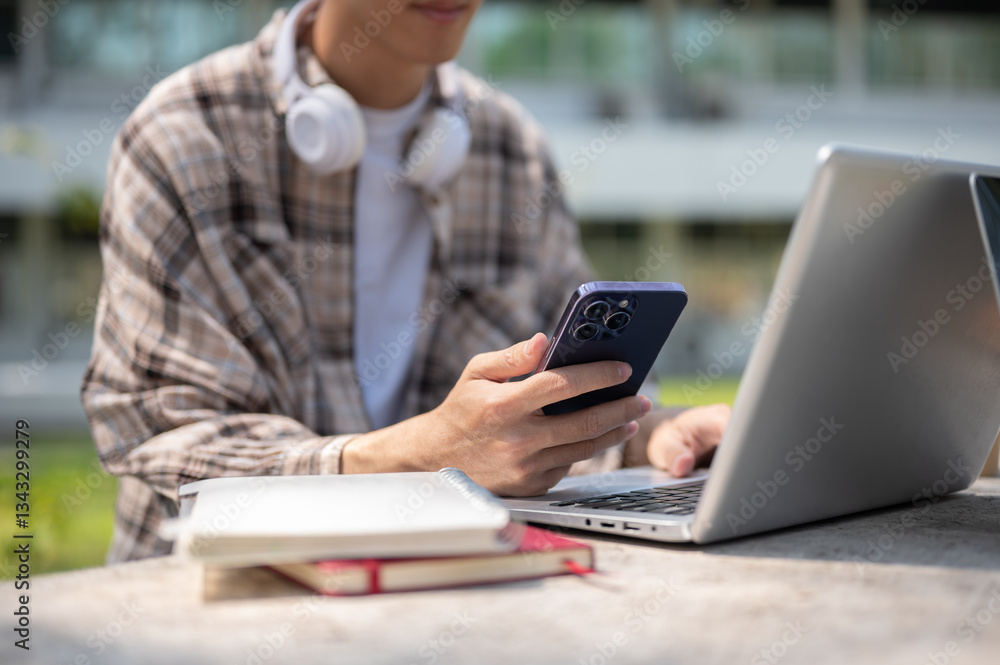 Close up of a man looking at his smartphone while sitting with a laptop at a concrete table in park. Close up of a man looking at his smartphone while sitting with a laptop at a concrete table in park.