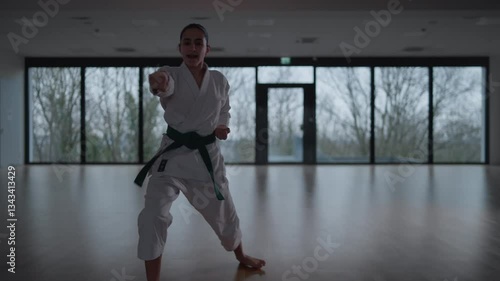 Woman training Karate in the dark, with big windows in the back