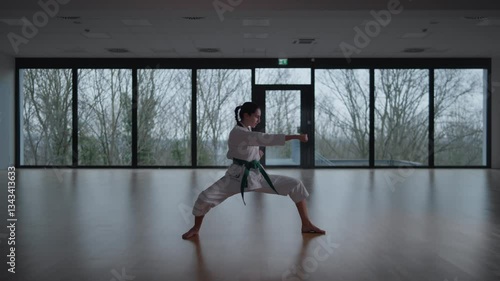 Woman training Karate in the dark, with big windows in the back