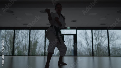 Woman training Karate in the dark, with big windows in the back