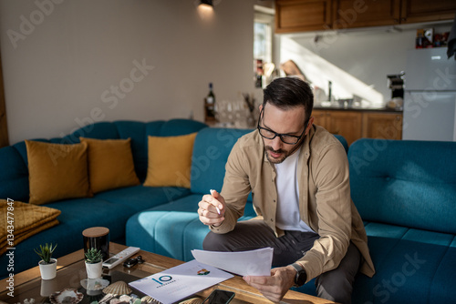 Принти на полотні Focused entrepreneur reviewing documents for tenth business anniversary at home
