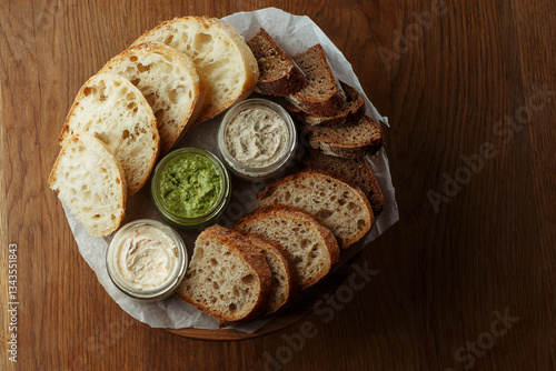 Obraz na płótnie Assorted artisan bread slices with three types of butter in glass jars on a rustic wooden table. A delicious selection of fresh bakery and butter for breakfast or snack. top view w salonie