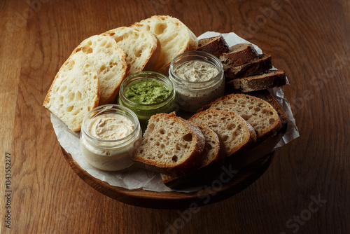 Obraz na płótnie Assorted artisan bread slices with three types of butter in glass jars on a rustic wooden table. A delicious selection of fresh bakery and butter for breakfast or snack. copy space w salonie