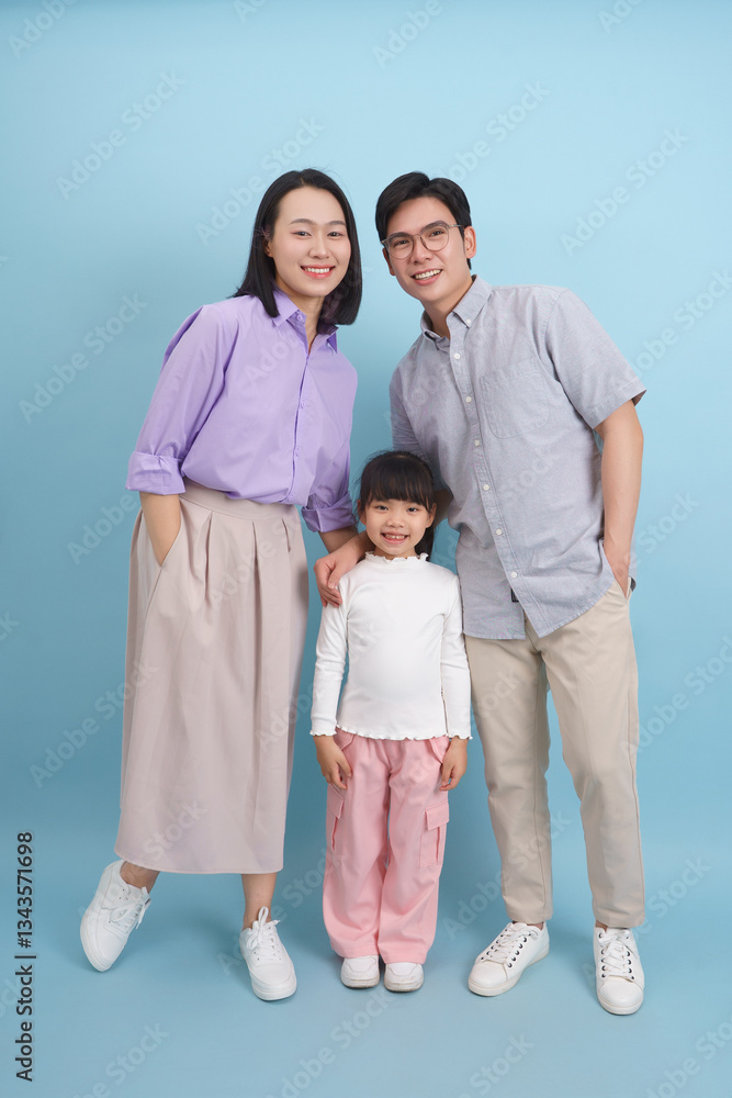 Happy family portrait featuring mother, father, and daughter in casual attire against a blue background Happy family portrait featuring mother, father, and daughter in casual attire against a blue background