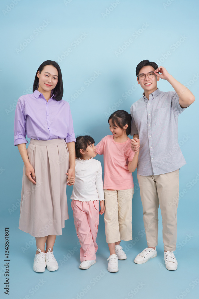 Family portrait featuring four members in casual attire against a light blue background Family portrait featuring four members in casual attire against a light blue background