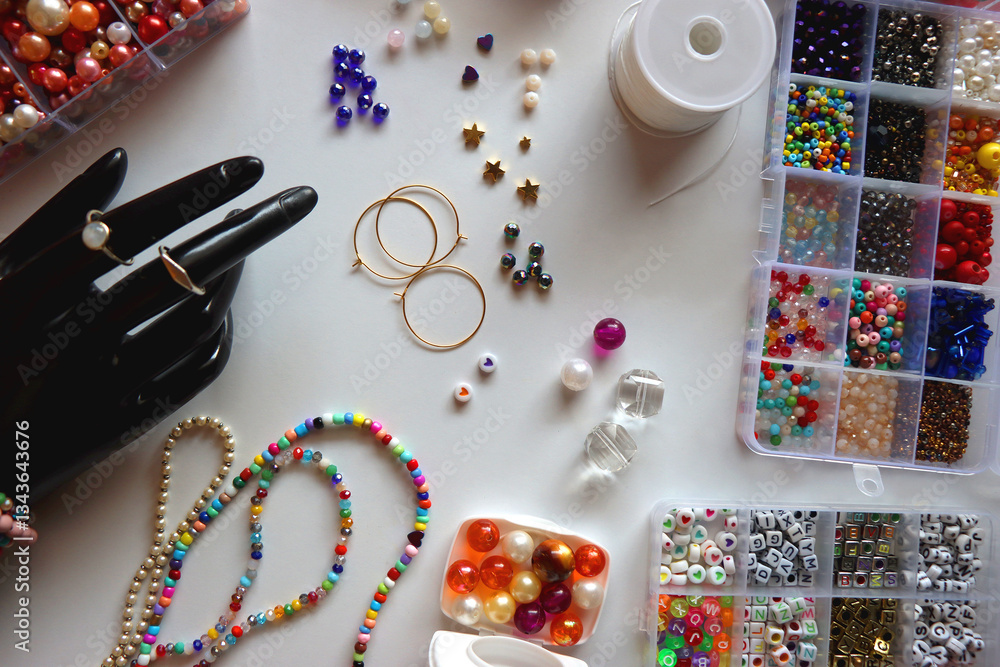 Hand figurine, colorful friendship bracelets, necklaces, various beads and DIY supplies on the table. Making jewelry at home. Flat lay.