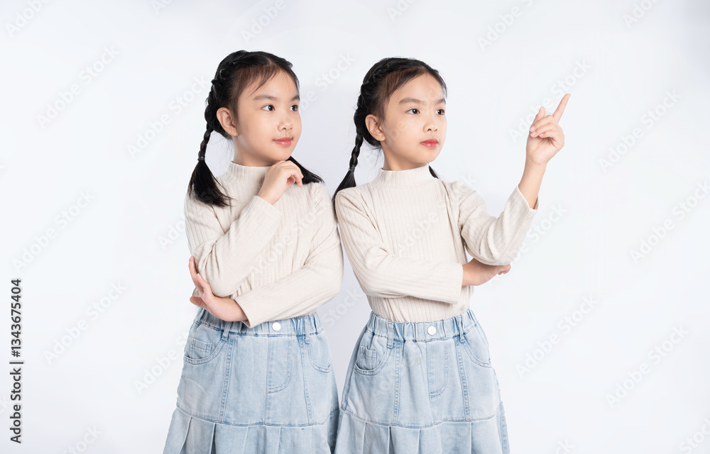 Adorable Asian twin girls striking a pose in matching outfits against a clean white backdrop. Adorable Asian twin girls striking a pose in matching outfits against a clean white backdrop.