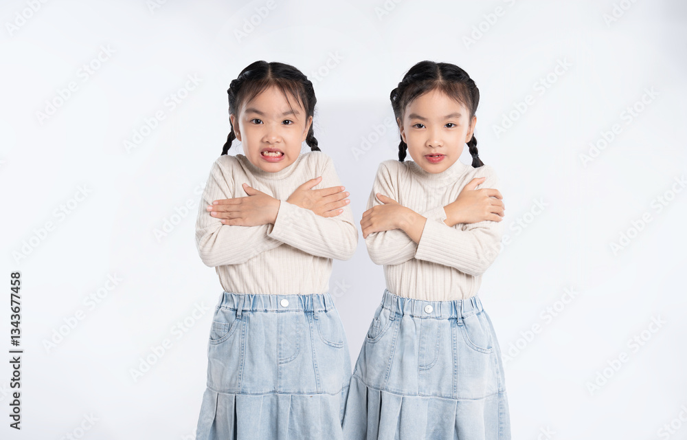 Twin sisters shivering, arms crossed. Same clothing. Isolated white background. Expressing coldness. Twin sisters shivering, arms crossed. Same clothing. Isolated white background. Expressing coldness.